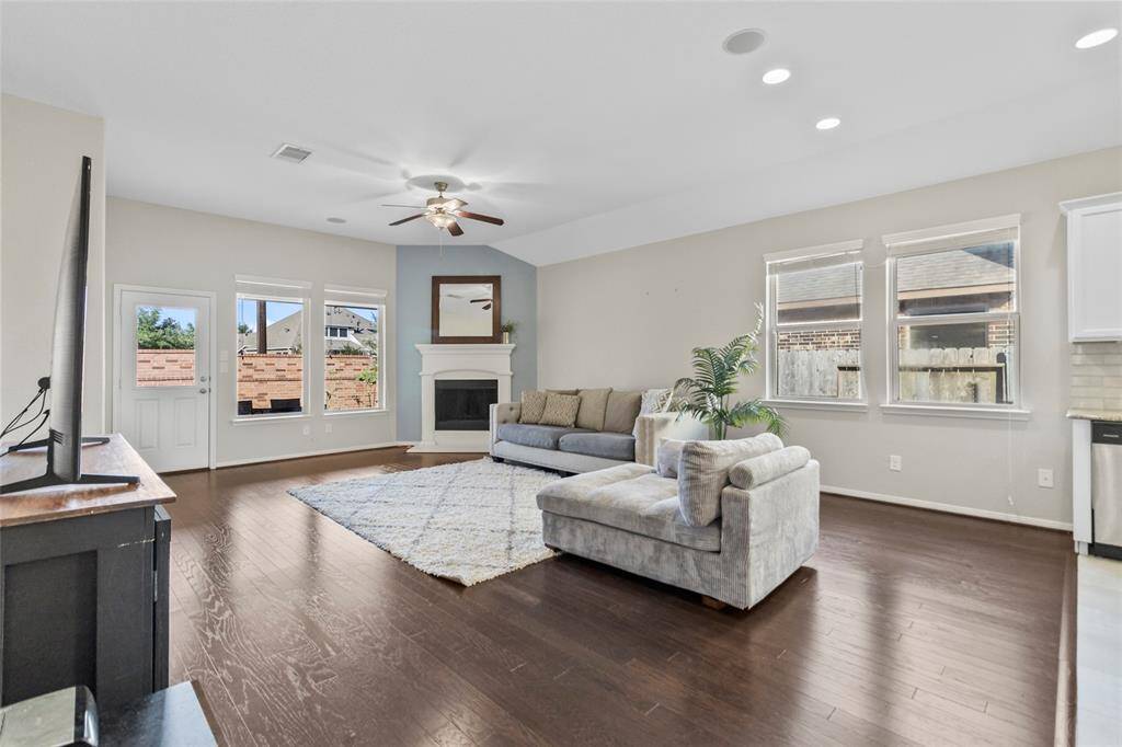 Natural light pours into your living room, highlighting the rich wood floors and cozy corner fireplace. The soft blue accent wall adds a calming touch, while the open layout makes this space perfect for both everyday living and entertaining.