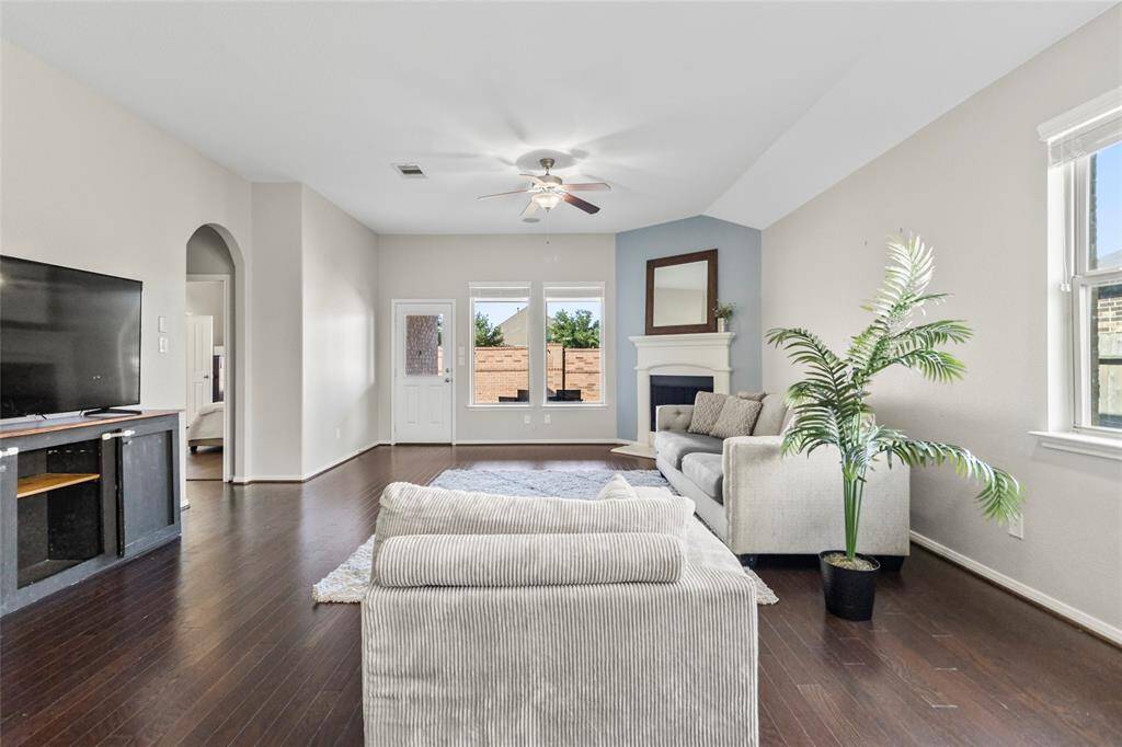 Anchored by a corner fireplace and wrapped in soft natural light, this living room balances warmth and elegance with ease. Crisp walls and rich wood flooring set the stage, while the vaulted ceiling adds a breezy, open feel. Your element of charm? That calming blue accent wall—it quietly frames the fireplace and brings the whole room to life.