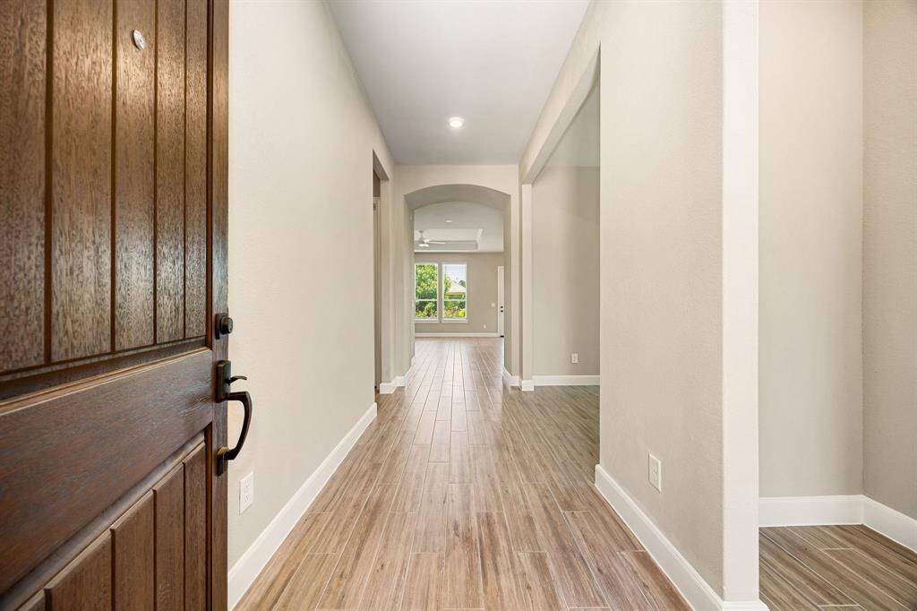 A very welcoming entryway with a solid wooden door opens to a long, bright hallway.
