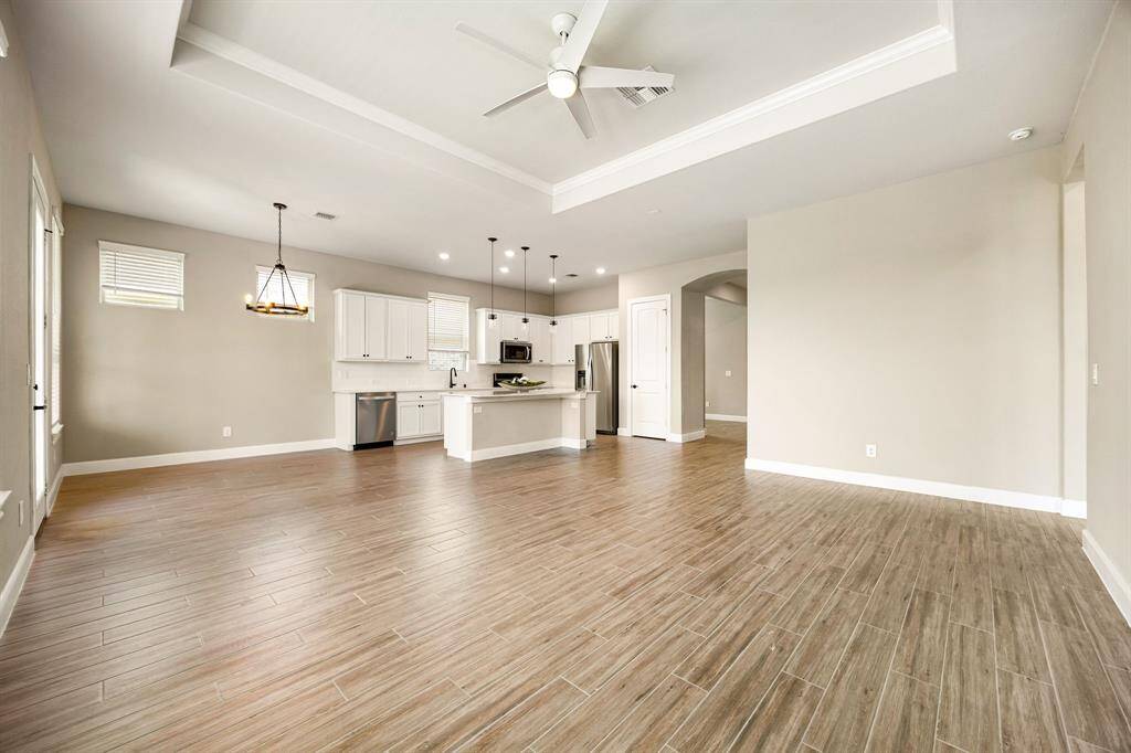 This open-concept living area features a view to the kitchen with white cabinets, stainless steel appliances, and a large island. The room is bright with recessed lighting, pendant lights, and a ceiling fan.