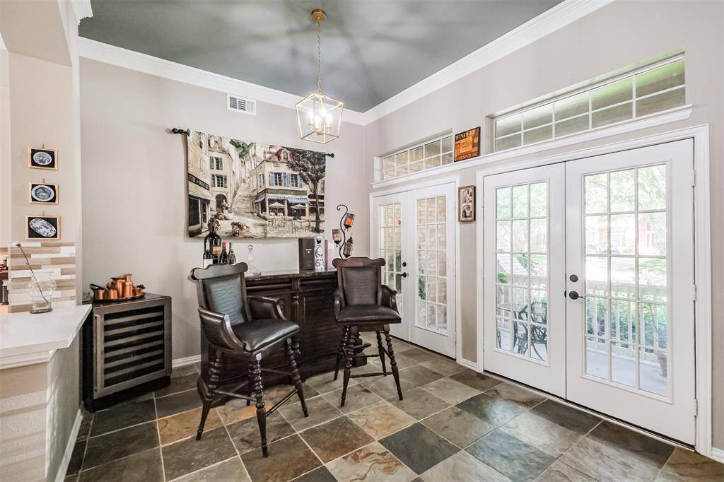 Discover a bright sunroom featuring elegant French doors, transom windows, slate flooring, modern light fixtures, crown molding, and a designer ceiling.