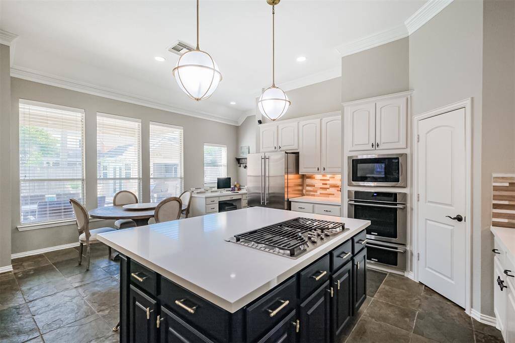 The updated gourmet kitchen features a large island with updated stainless cooktop and downdraft, seating area, and soaring ceilings.
