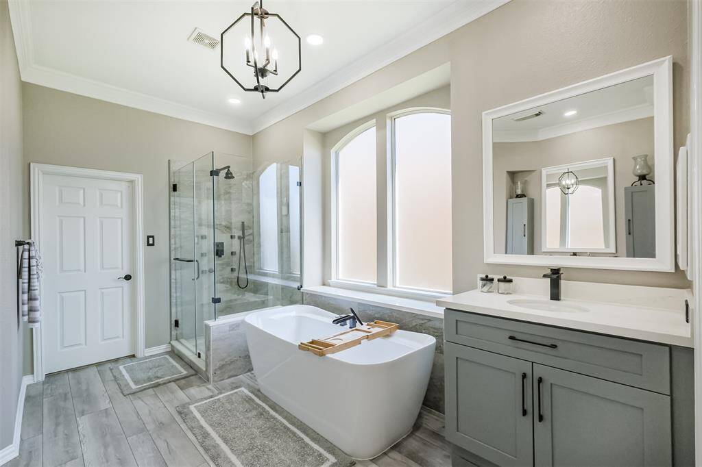 Experience luxury in the modern primary bathroom featuring a freestanding soaking tub, quartz countertops, sleek painted cabinets, tile flooring, and a frameless glass shower.