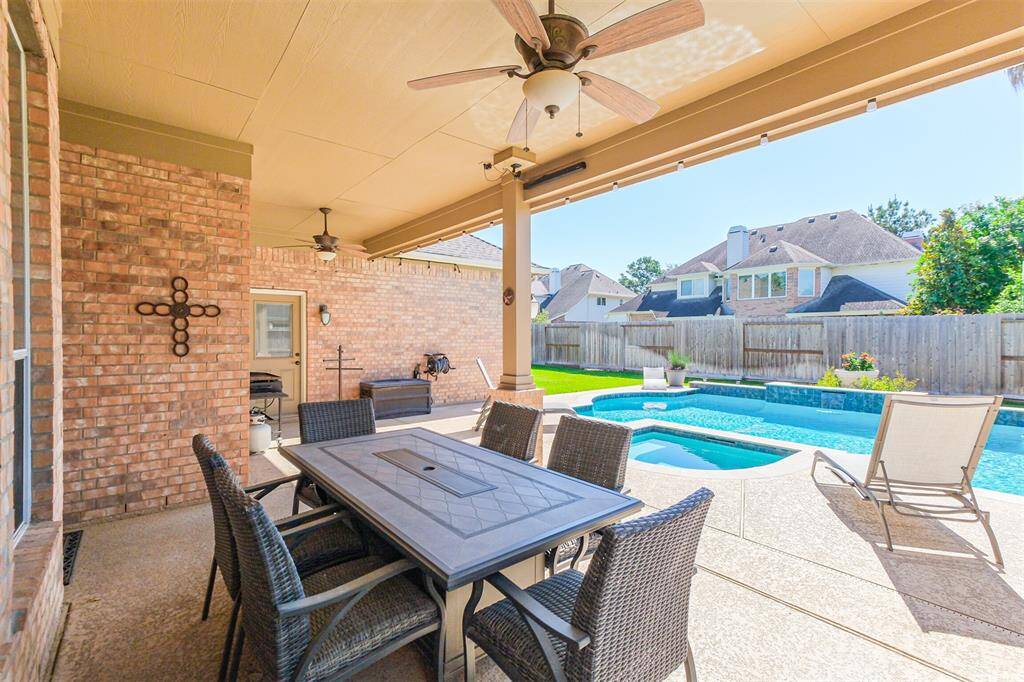Enjoy the expansive covered patio overlooking a sparkling pool, hot tub, and lush grassy yard.
