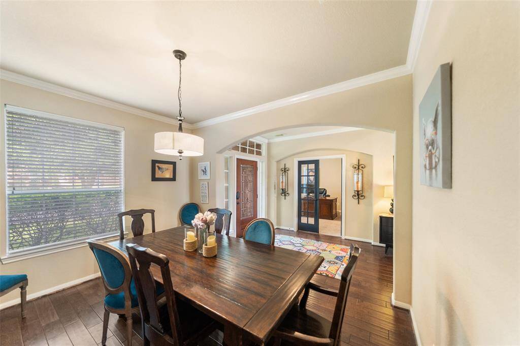 This inviting dining room features warm wood floors and stylish lighting. It opens to an adjacent office through elegant glass doors, creating a seamless flow.