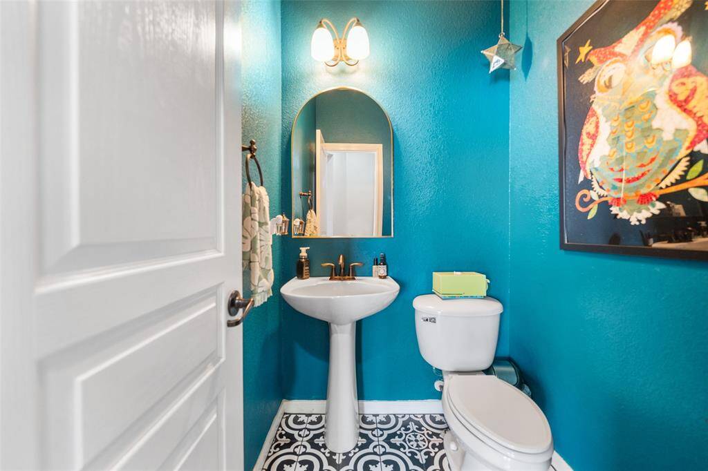 This is a vibrant half-bathroom featuring bold turquoise walls, a pedestal sink, toilet, and stylish black-and-white patterned flooring.