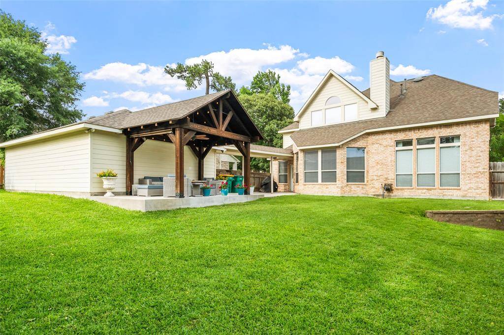 Spacious backyard featuring a well-maintained lawn, wooden fencing, and a cozy covered patio area with seating. Perfect for outdoor entertaining and relaxation.