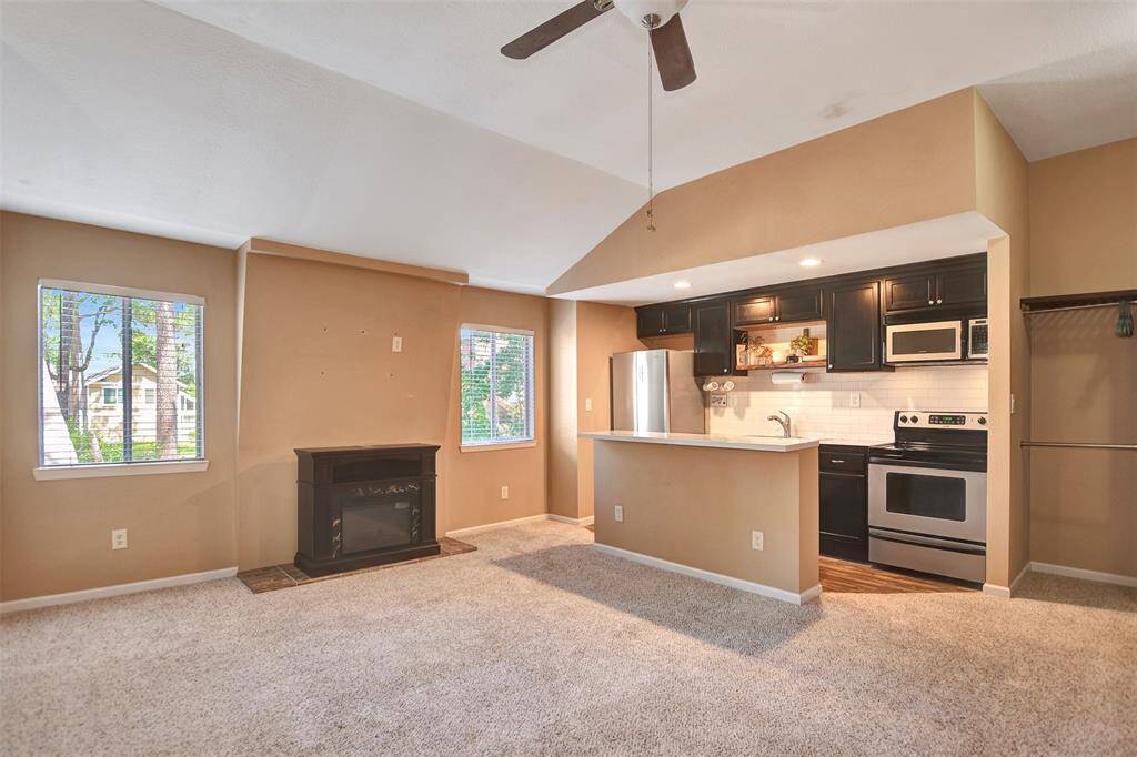 It features a compact kitchen with stainless steel appliances, dark cabinetry, and a convenient breakfast bar. The room has ample natural light from two windows and includes a small fireplace for added warmth and charm.