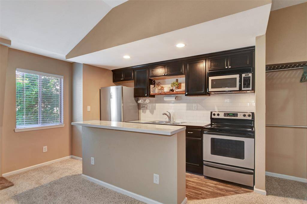 Modern kitchen with stainless steel appliances, dark cabinetry, and a sleek subway tile backsplash. The open layout features a breakfast bar, while natural light pours in through a nearby window, creating a cozy and inviting space.