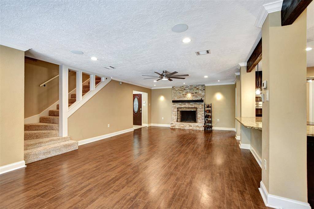 This spacious living area features elegant hardwood floors, and a  cozy stone fireplace. The open layout includes a staircase leading upstairs and a pass-through to the kitchen, creating a warm and inviting atmosphere.