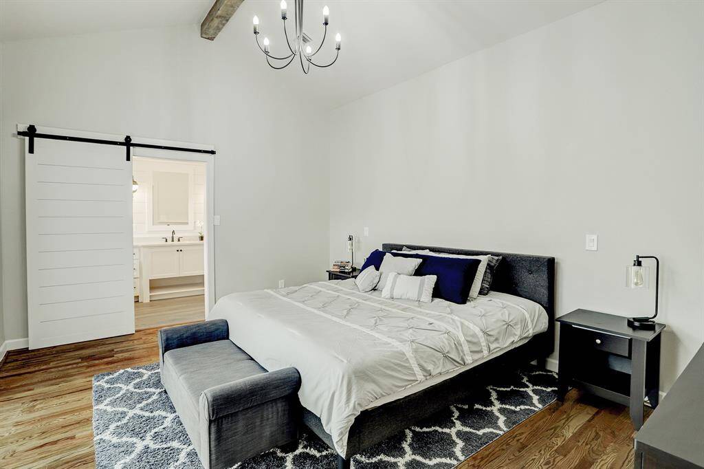 The primary bedroom has wood floors, sliding doors to access the back patio, chandelier, and a vaulted ceiling with beam.