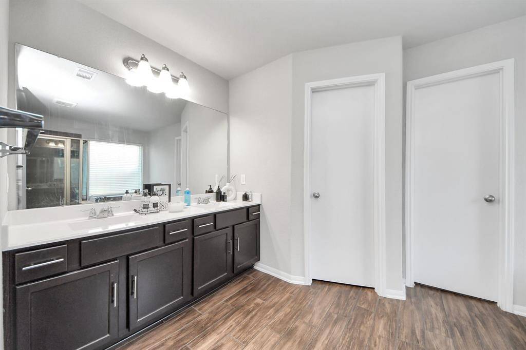 Dual vanity, separate soaking tub and glass-enclosed shower with wood-look tile flooring.