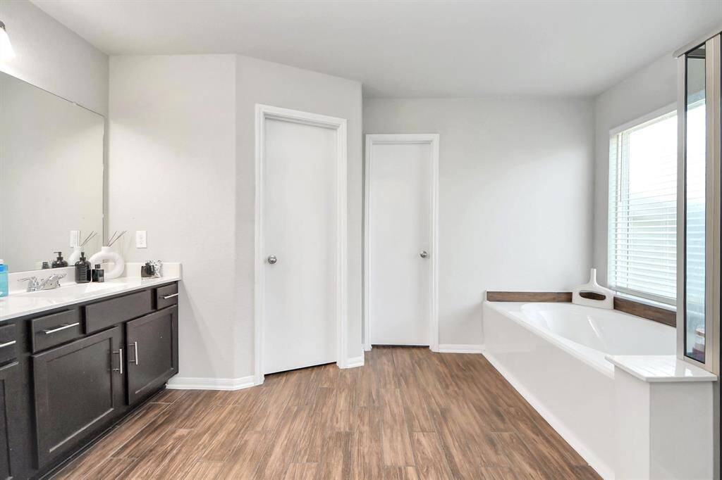 Dual vanity, separate soaking tub and glass-enclosed shower with wood-look tile flooring.