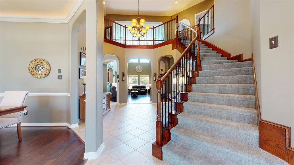 Step into the heart of the home where a stunning sweeping staircase immediately captures attention with its rich wood accents, wrought-iron spindles, and graceful curve. This architectural centerpiece creates a dramatic focal point in the two-story foyer, enhanced by soaring ceilings and an abundance of natural light. Overlooking the grand entry, the upstairs landing adds a sophisticated touch and a sense of openness—perfect for welcoming guests in style.