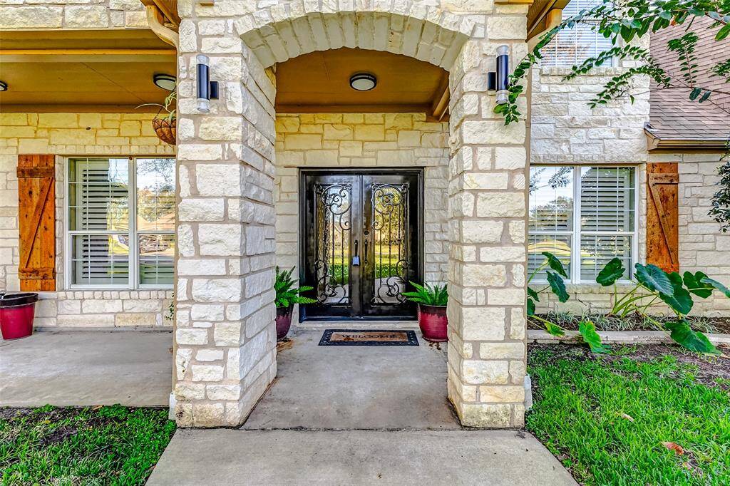 The grand entryway of this home features stunning wrought iron double doors framed by a stately stone archway. Accented by vibrant greenery and elegant light fixtures, this inviting porch exudes timeless charm. From the spacious porch, you can enjoy conversations with yourneighbors and family, while taking in the gorgeous views of the front yard.