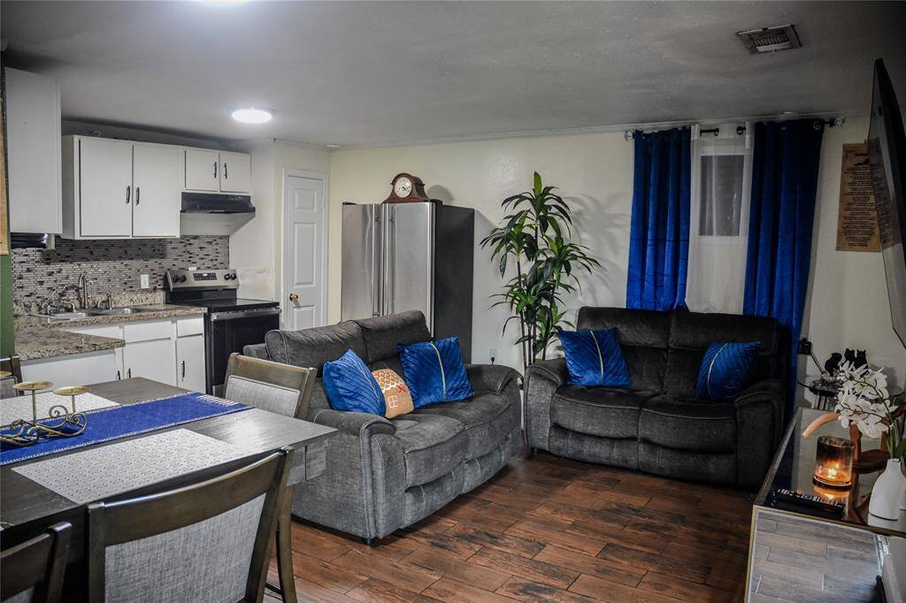 Open living room with hardwood-style tile flooring flowing into a granite-top kitchen with stainless appliances.