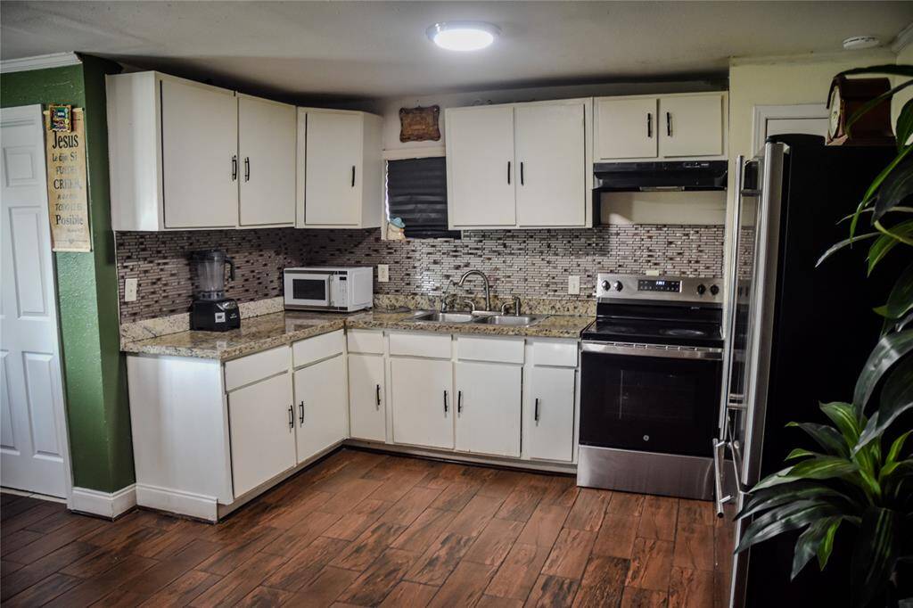 View of the kitchen with white cabinetry, granite countertops, and decorative mosaic backsplash.