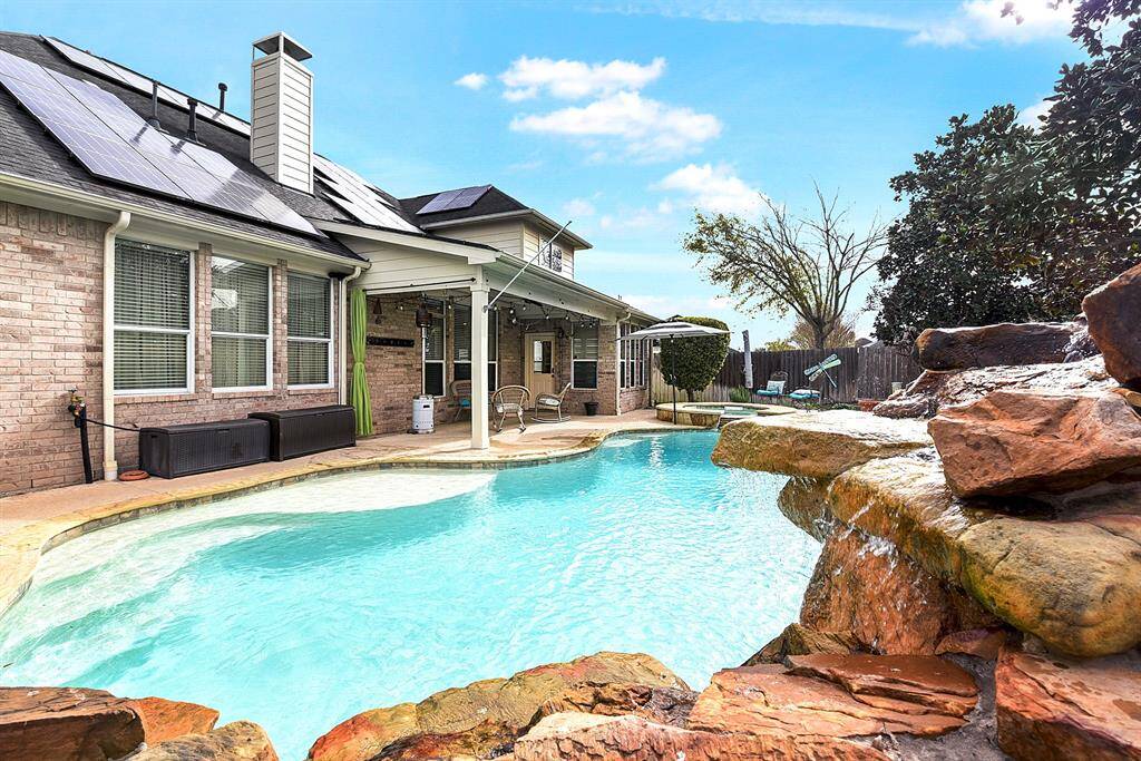 Another view highlights this private backyard oasis, featuring a beautiful waterfall and jumping rocks. The pool includes a shallow sun deck, perfect for lounging, relaxing, and staying cool during the hot summer months.