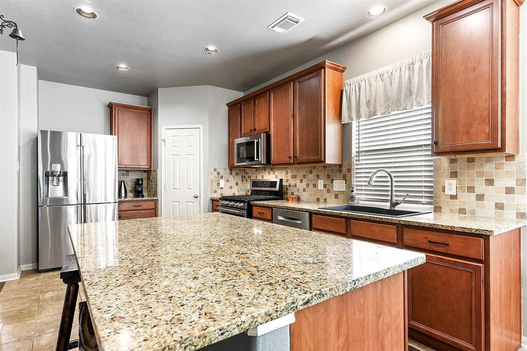 Another view of this gorgeous kitchen showcases recessed lighting, a gas stove, and a large pantry, providing both style and functionality. Adjacent to the refrigerator, you’ll find the perfect coffee nook—an ideal spot to start your day or unwind with your favorite brew.