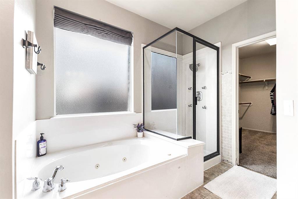 The luxurious primary en suite features a large soaking jetted tub, perfect for relaxing after a long day. It also offers a separate stand-up glass shower with multiple showerheads and bench seating, creating a spa-like experience right in your home.