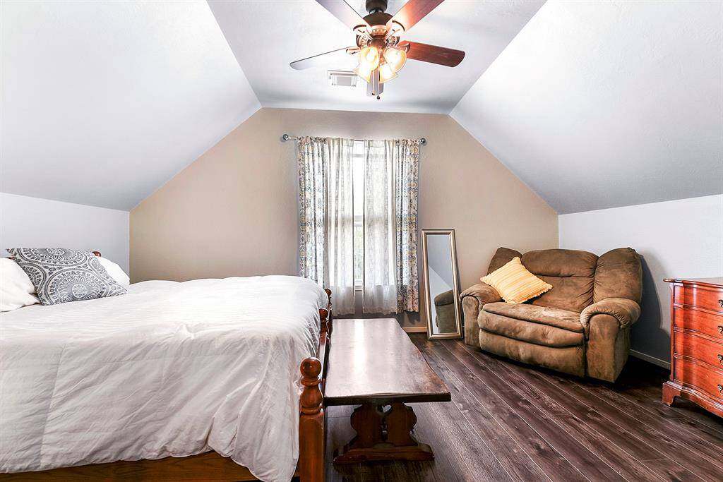 This large bedroom features a ceiling fan and plenty of space for an additional seating area, along with the same wood flooring.