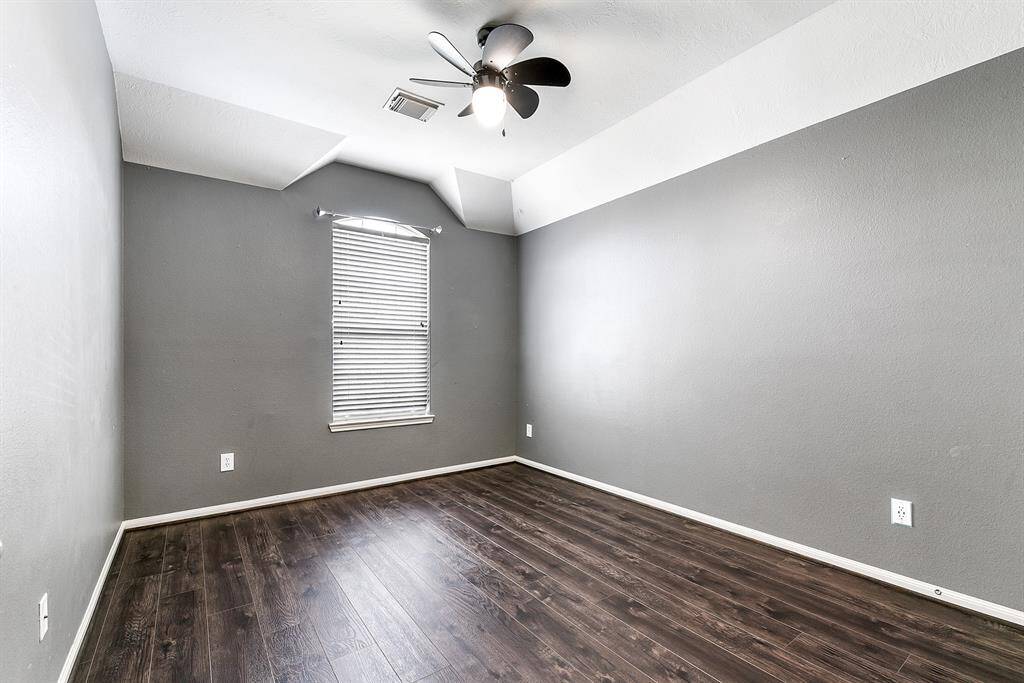 The upstairs guest bedroom features a drop-down ceiling fan, wood flooring, and window treatments.