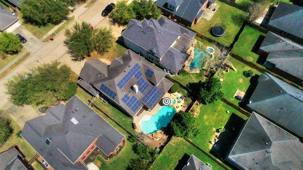 An aerial view showcases the home’s solar panels, large swimming pool, and hot tub, complemented by an extended patio. This setup highlights the property’s energy efficiency and outdoor entertainment features, creating the perfect space for relaxation and gatherings.