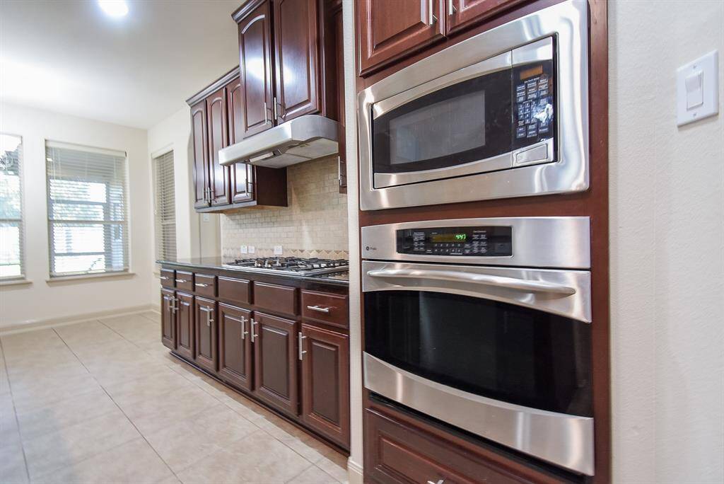 Modern stainless steel appliances, including a built-in microwave and oven. Rich wood cabinetry offers ample storage, complemented by a sleek gas cooktop and vent hood.