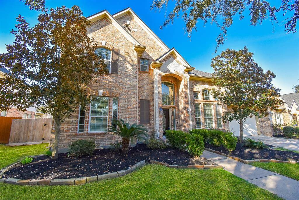 This is a beautiful two-story brick home with large windows, a well-maintained front yard, and mature trees.