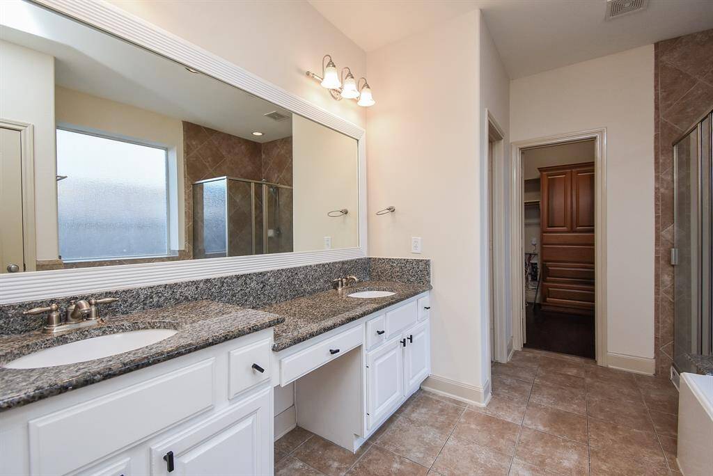Modern primary bathroom featuring dual sinks with granite countertops, a large mirror, and elegant lighting.