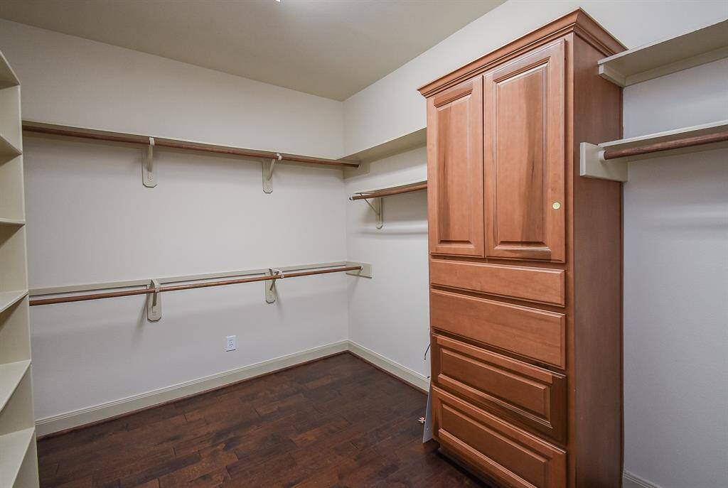 Spacious walk-in closet with ample shelving and hanging space, featuring a built-in wooden cabinet for added storage.