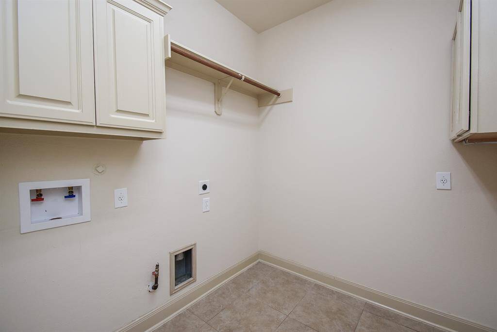 Spacious laundry room featuring upper cabinets for storage, washer and dryer hookups, and tile flooring.