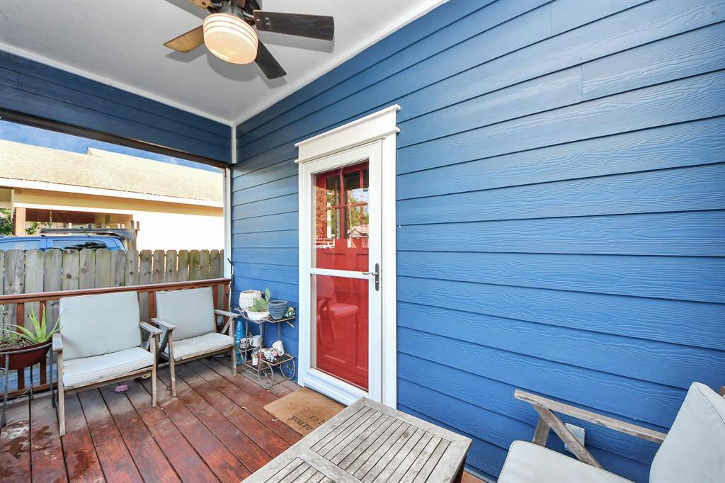 Charming porch with blue siding and a red door, featuring comfortable seating, a ceiling fan, and a pull-down shade, perfect for relaxing outdoors.
