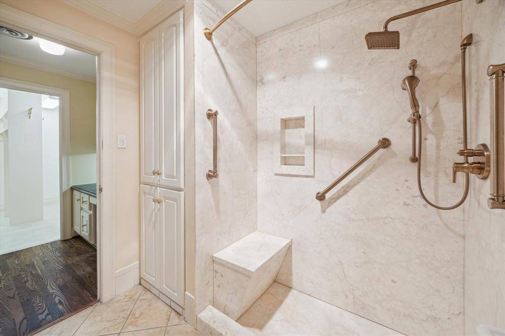 Primary Ensuite Bathroom with tile flooring and step-in shower with grab bars. Linen cabinet on left and single vanity with Phylrich faucet not shown on opposite side.