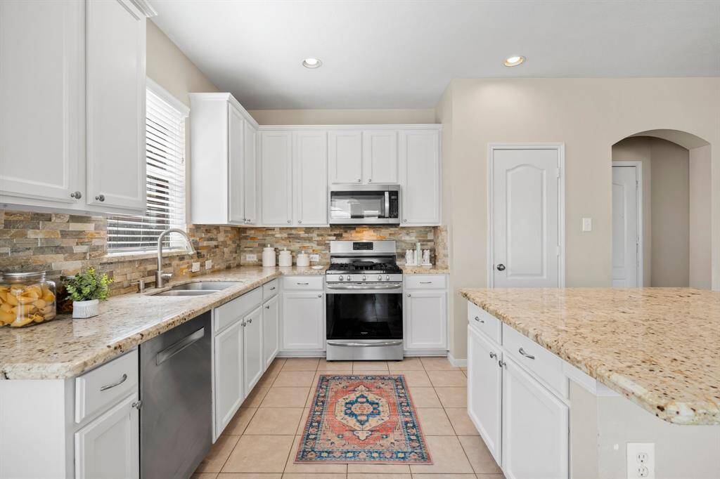 Granite countertops, stone backsplash, white cabinets, stainless steel appliances and gas stove make this kitchen a fantastic place to prepare meals.
