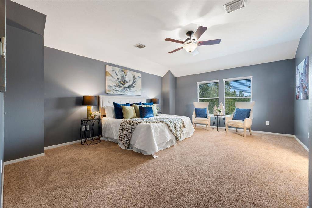 Large primary bedroom is located upstairs and includes large windows and ceiling fan.