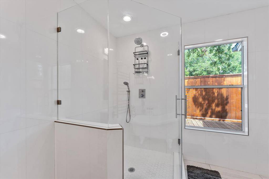 The walk-in shower is framed by clean tilework and natural light from the nearby window, creating a bright and refreshing start to your day.