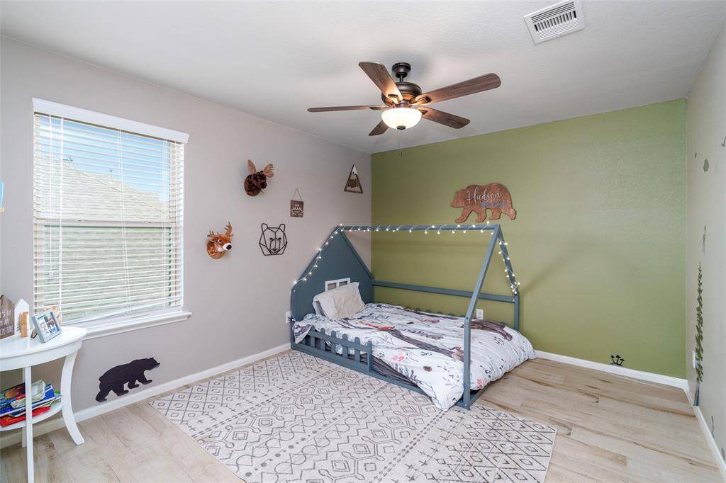 This stylish bedroom features engineered wood flooring, a ceiling fan for added comfort, and a custom accent wall that adds a unique touch.