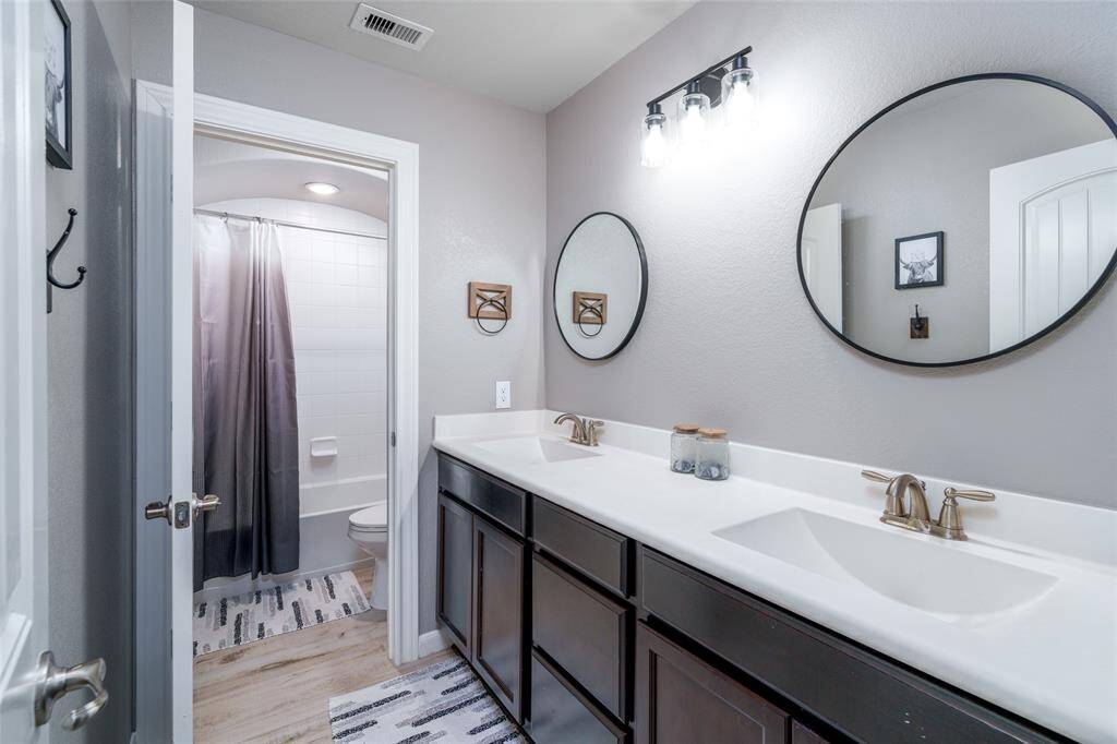 This bathroom offers a practical shower/tub combo and toilet, thoughtfully separated from the elegant double sink vanity featuring stylish framed round mirrors for added charm and convenience.