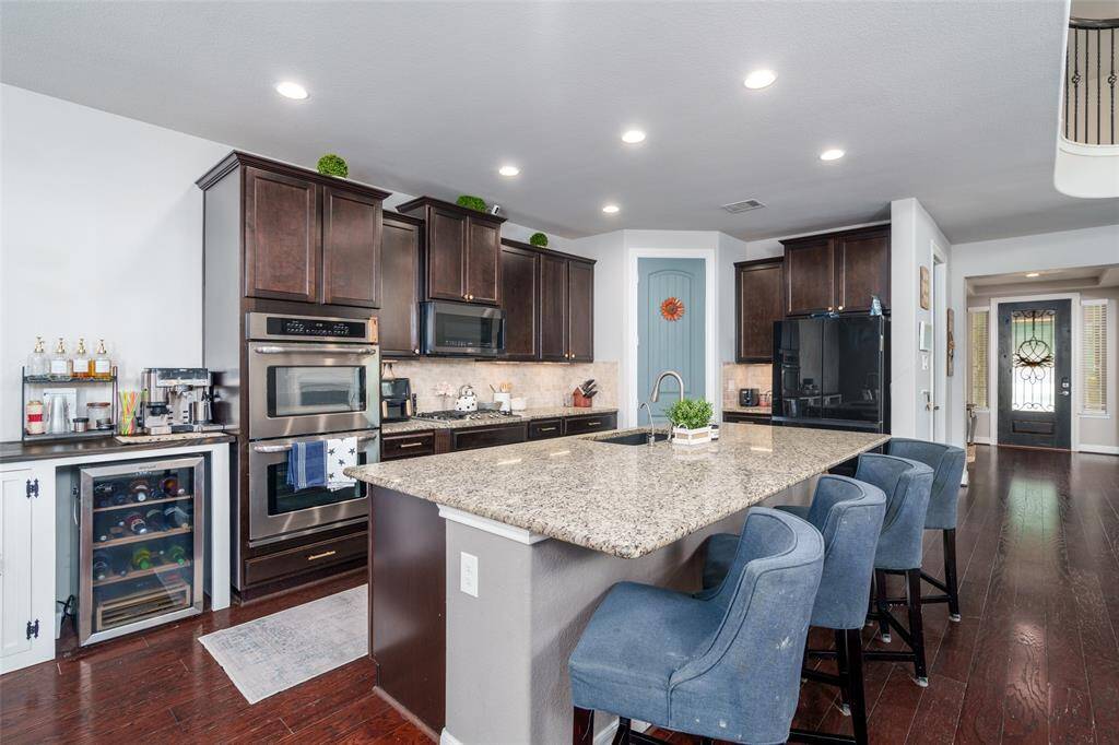 The kitchen is a chef’s dream, showcasing rich dark-stained cabinets, sleek granite countertops, double ovens, and a spacious kitchen island perfect for cooking, dining, or entertaining.