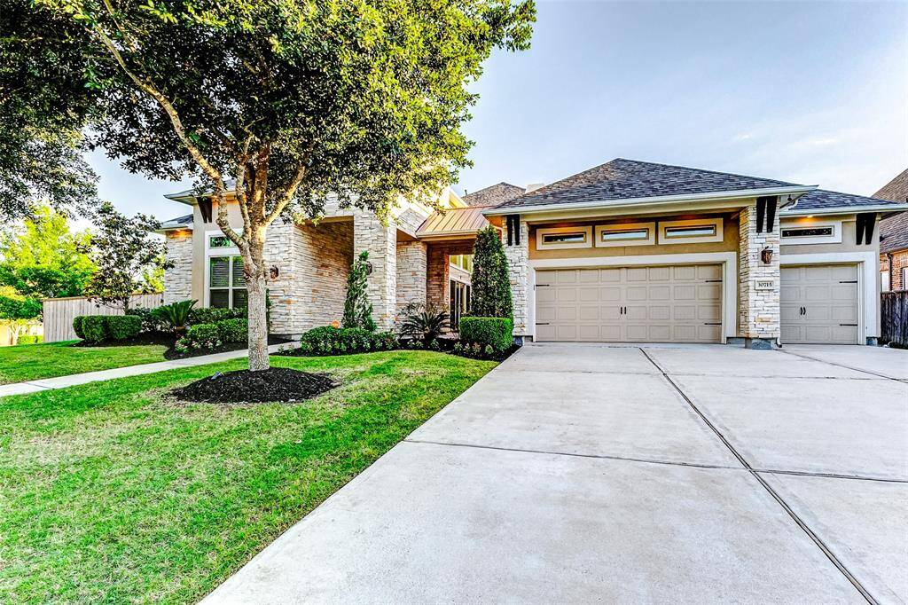 A spacious double-wide driveway gracefully expands to a triple width, offering ample parking and leading to a four-car garage. One bay is set apart, ideal for a private vehicle, workshop, or additional storage.