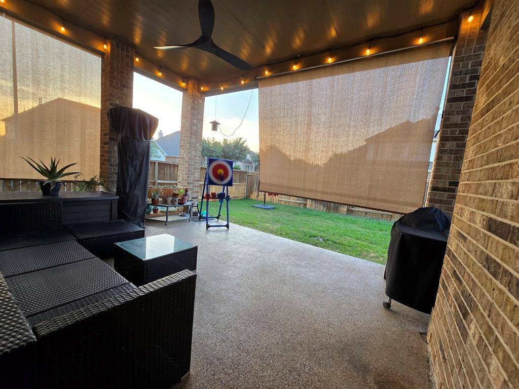 This inviting covered patio is equipped with a pair of roll-down sunshades to control sunlight and a ceiling fan for added comfort.