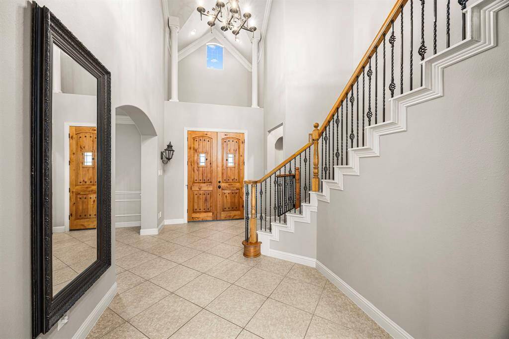 Looking back toward the Foyer, take note of the elegant oil-rubbed bronze 8-light chandelier, intricate crown molding, and the landing above the front door, accentuated by a beautifully arched window. Stately pillars add architectural interest, enhancing the grandeur of this stunning entrance.