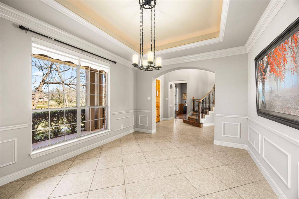 This view from the opposite side of the Dining Room highlights its prime position just off the Foyer, showcasing the elegant oil-rubbed bronze chandelier, detailed chair molding, and abundant crown molding. The large bay window offers a stunning view of the expansive front yard, filling the space with natural light and enhancing its refined charm.