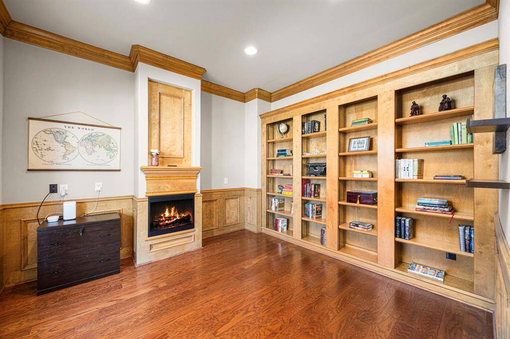 The Home Office is truly grand, featuring rich wood floors, extensive custom-built cabinetry, and a hidden 'safe room' tucked behind the shelving. An elegant electric fireplace adds warmth and sophistication to the space.
