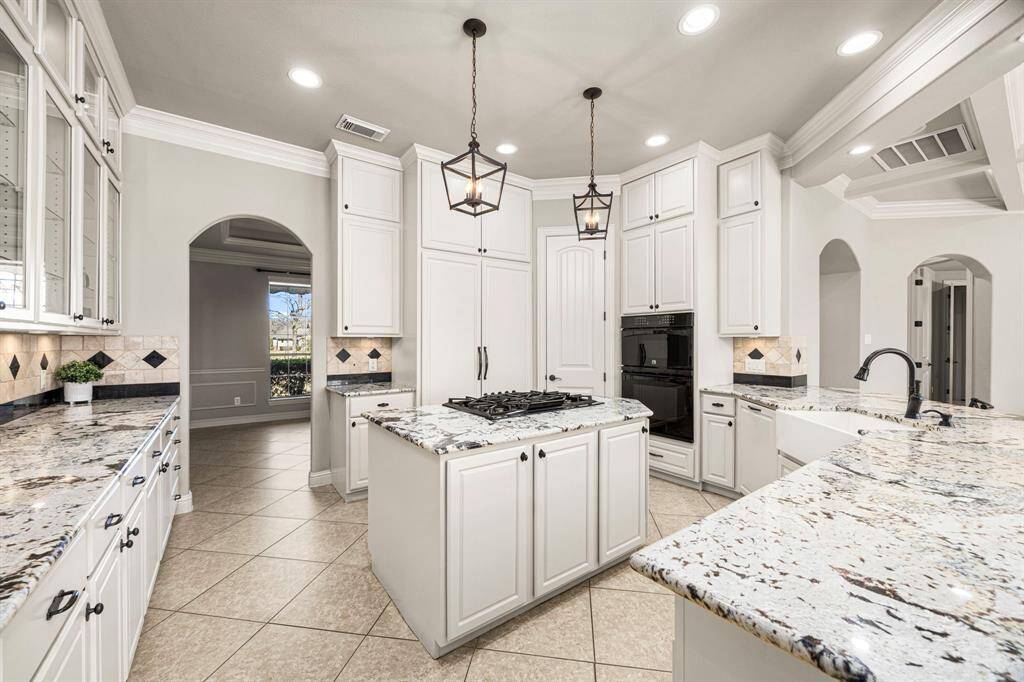 The center Island houses a 5-burner gas cooktop with an electric control downdraft, providing both convenience and efficiency. Above, two elegant birdcage pendant lights add a stylish touch, while built-in storage enhances functionality. The Kitchen also features a cabinet-front built-in Thermador refrigerator and dishwasher, seamlessly blending with the off-white cabinetry for a sleek and cohesive look. High-end finishes and thoughtful design make this space both beautiful and highly functional.