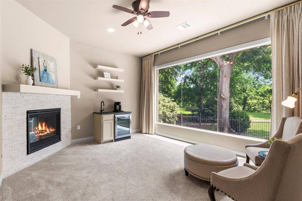 This Flex Room, connected to the Primary Bedroom, exudes luxury and versatility. It features expansive seamless windows adorned with gorgeous window treatments, allowing natural light to fill the space while enhancing privacy. A cozy gas log Fireplace with a brick surround and wood mantel adds warmth, while a built-in coffee or wine bar with an undermount sink and beverage refrigerator provides the perfect touch for relaxation or entertaining.