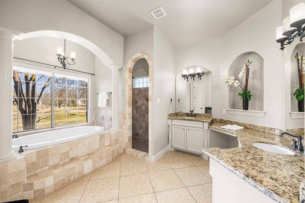The Primary Bath offers a spa-like retreat, featuring a large soaking tub set beneath a beautiful set of windows, complete with an elegant chandelier above. Luxurious granite countertops, double undermount oval sinks, and a spacious shower with a built-in bench and oil-rubbed bronze fixtures enhance the elegance and functionality of this serene space.