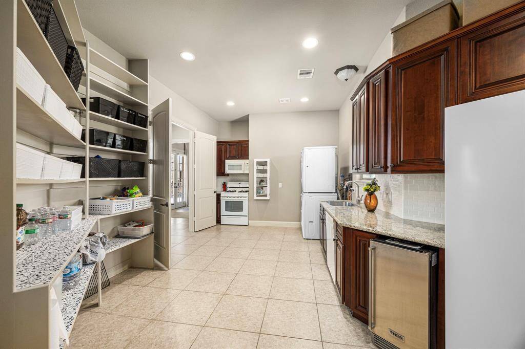 This incredible multi-purpose space serves as both a Laundry Room and a secondary Kitchen, featuring a 4-burner gas range, dishwasher, ice maker, and space for a refrigerator or freezer. Located just outside the Guest Suite, it provides added convenience and ample overflow storage, making it perfect for extended stays or entertaining.