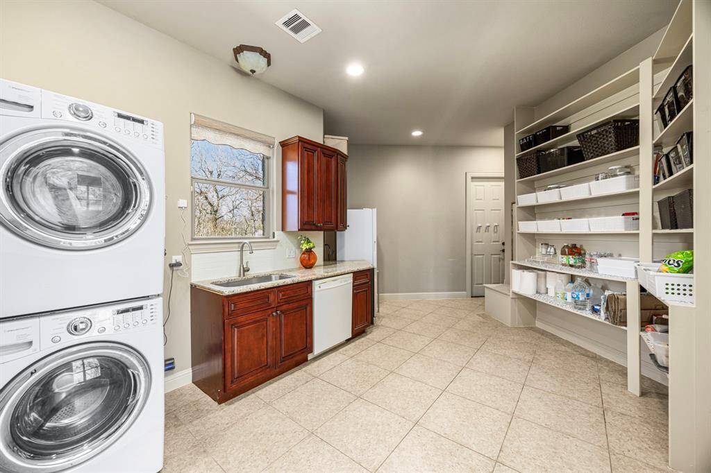 Another view of the multi-purpose space highlights its convenient access door to the 3-Car Garage, making it easily accessible for daily use. With ample shelving for storage and durable 18x18 tile floors, this space is both functional and well-designed. Please note the Washer/Dryer/Freezer are excluded.